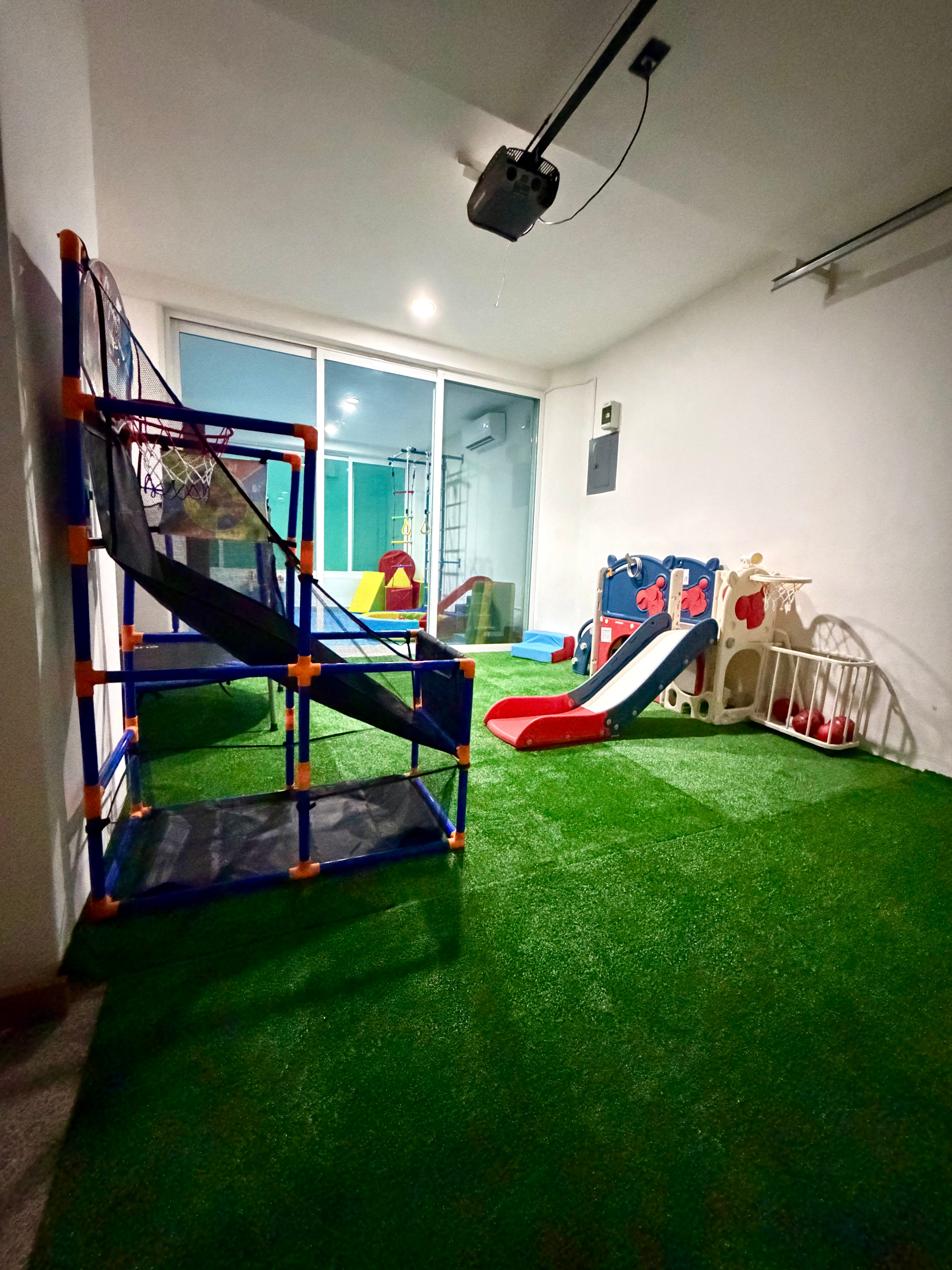 Zona de movimiento de la ludoteca Ludo Mix en Puerto Vallarta, con escalera sueca, tobogán, piscina de pelotas y área de pasto sintético